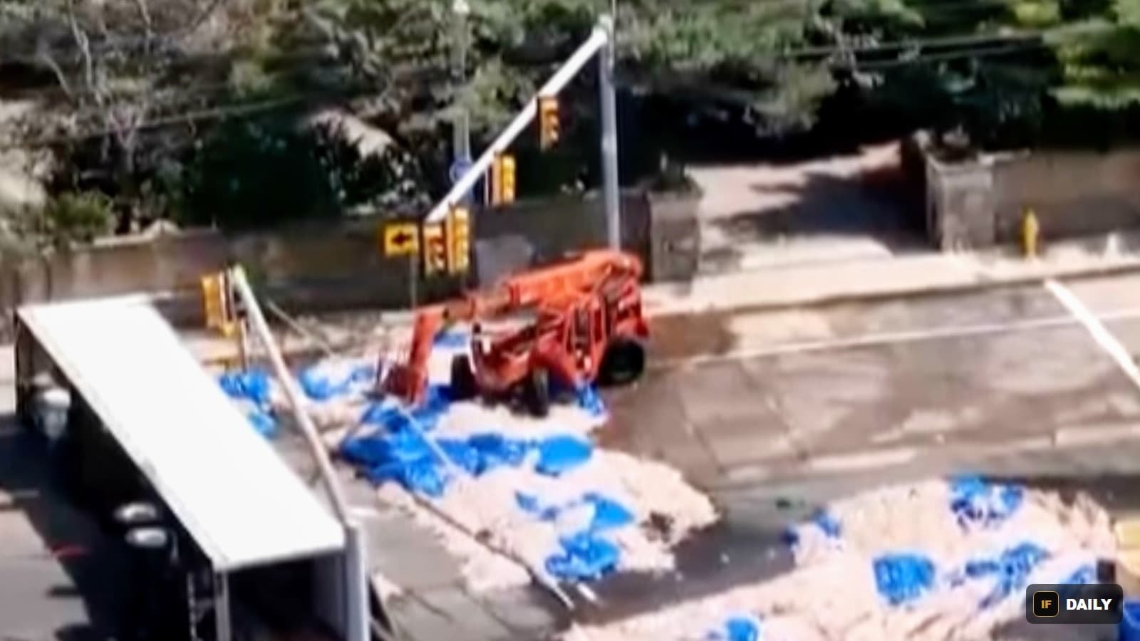 Aerial view of a road covered in spilled squid and blue tarps, with a crane vehicle beginning cleanup