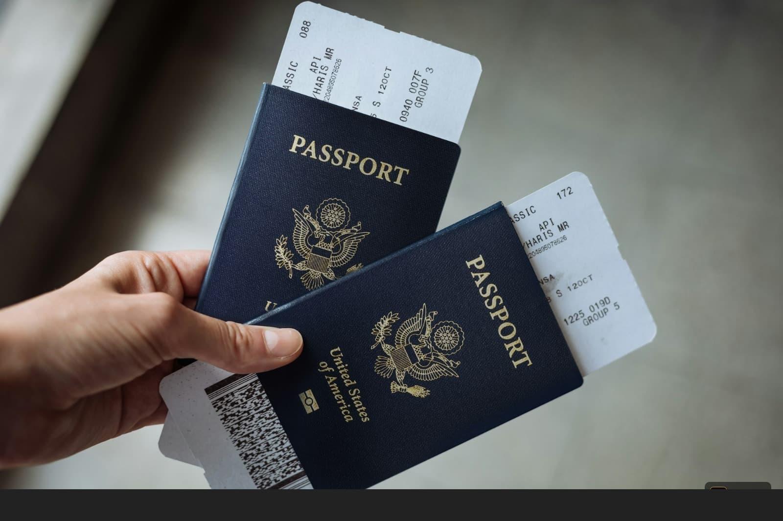A hand holding two US passports with airline boarding passes tucked inside them