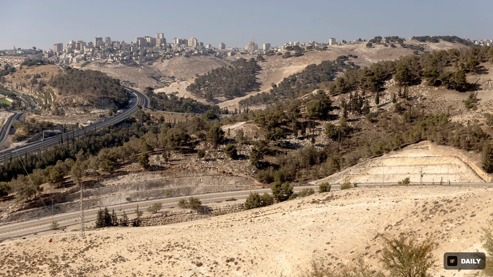 An aerial view of hills, a highway, and a Palestinian city in the occupied West Bank near Jerusalem